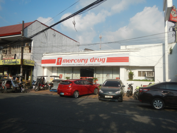 Eine belebte Straßenszene mit Fahrzeugen, Gebäuden, Strommasten und einer Mercury-Apotheke im Vordergrund.