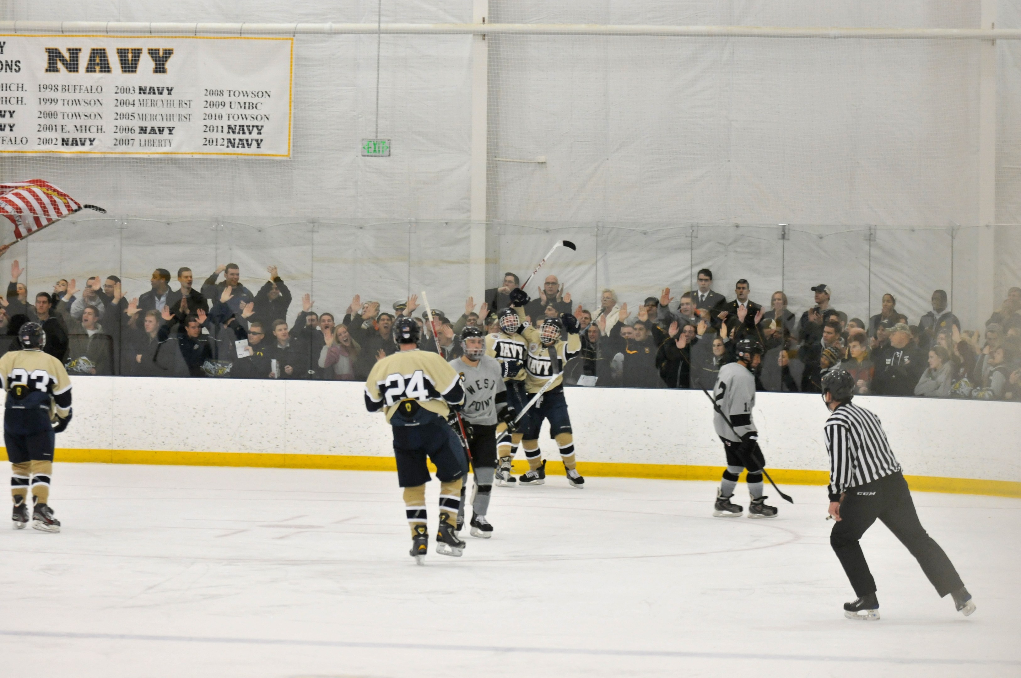 Gruppe von Menschen, die Eis-hockey auf einem Eis-hockeyfeld spielen, mit Zuschauern auf den Tribünen und einem Banner im Hintergrund.