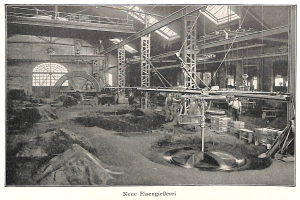 Schwarzes und weißes Foto einer Fabrik mit Arbeitern, die an einer Maschine arbeiten, umgeben von Metallstangen und Pfählen, beschriftet mit "Neue Eisenglebeerei, die erste Fabrik in Deutschland."