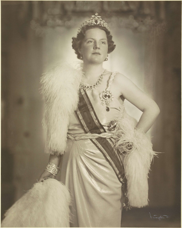 Schwarzes und weißes Foto von Queen Elizabeth II in einem Kleid und einer Krone, mit unscharfem Hintergrund und Text unten.