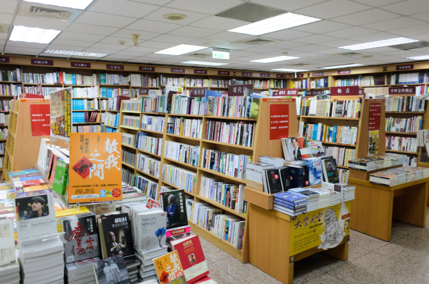 Ein gut organisierter Buchladen mit zahlreichen Büchern auf Regalen und Tischen, Informationsschildern auf dem Boden und Deckenbeleuchtung.