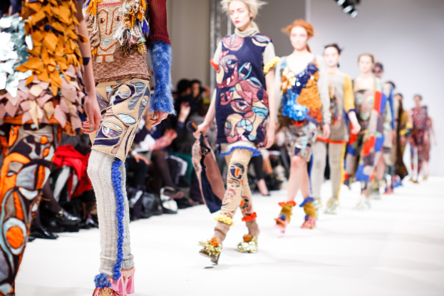 Eine Gruppe Von Frauen Geht Den Laufsteg Bei Der London Fashion Week Herunter, Mit Sitzenden Zuschauern Und Bühnenbeleuchtung Im Hintergrund.