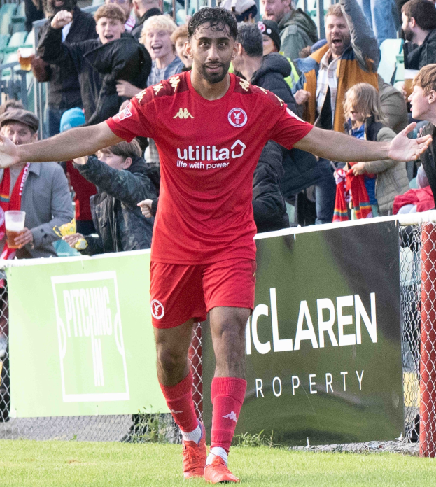 Ein Fußballspieler in roter Uniform rennt mit ausgebreiteten Armen auf einem Feld, umgeben von Zuschauern hinter einem Zaun, mit einem "Middlesbrough FC v Swansea City - Sky Bet Championship"-Schild im Hintergrund.