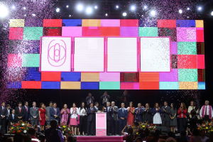Gruppe von Menschen auf einer Bühne mit einem Podium, Blumenarrangements auf beiden Seiten, Kameras in der Hand und ein großer Bildschirm mit Lichtern während der Eröffnungszeremonie des 2018 China International Film Festival.
