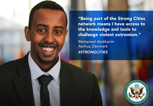 Ein Mann im Anzug und Krawatte lächelt in die Kamera mit einem Logo und Text auf der rechten Seite, der besagt "Teil des starken Städtenetzwerks zu sein bedeutet, Zugang zu Wissen und Werkzeugen zu haben, um gewalttätigen Extremismus in Frage zu stellen", mit einem unscharfen Hintergrund.