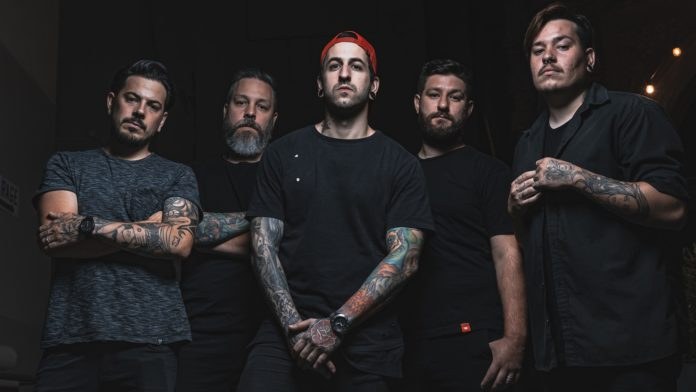 Eine Gruppe von Männern, die in einem dunklen Raum während eines Interviews stehen, von rechts beleuchtet, wahrscheinlich für die Band Avenged Sevenfold.