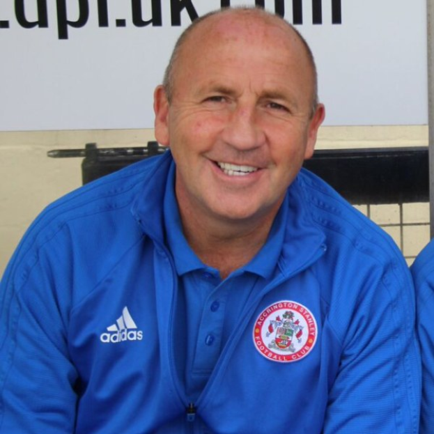 Zwei Männer in einem Raum, einer in einem blauen Jackett neben dem anderen, mit einer Wandtafel im Hintergrund.
