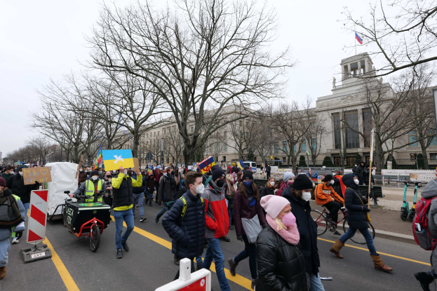 Eine große Gruppe von Menschen nimmt an einer Protestdemo in Washington, D.C. am 21. Januar 2020 teil und marschiert eine Straße entlang mit Schildern, Bannern und Fahrrädern vor einer Kulisse von Schildern, Bäumen und einem klaren blauen Himmel.