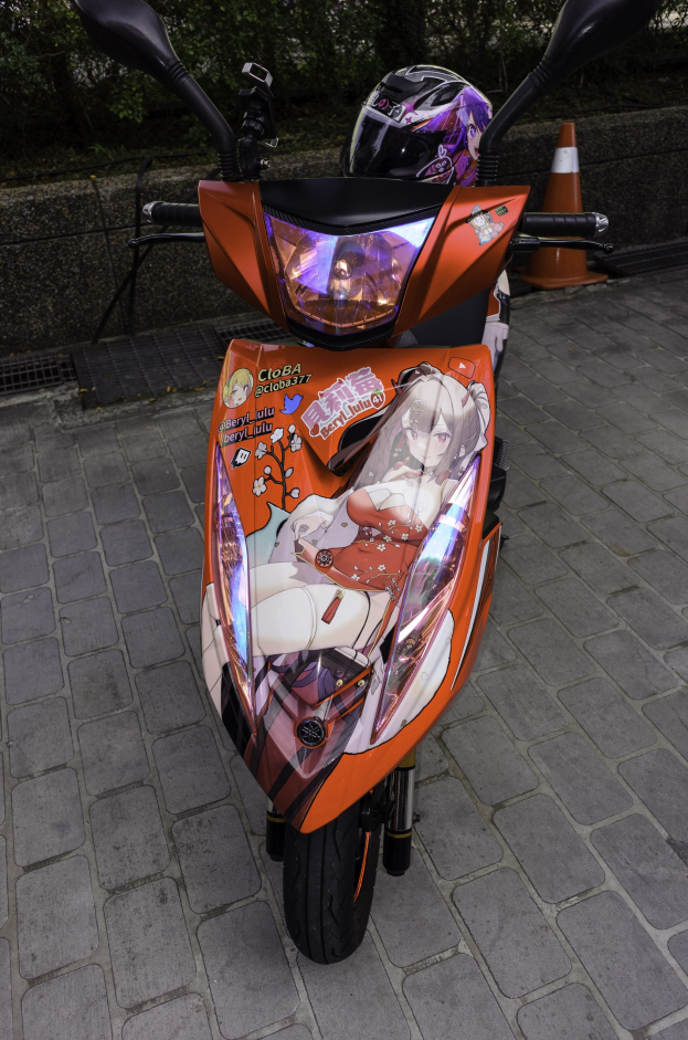 Ein oranger Roller mit Helm darauf auf einer Straße geparkt, mit einem Verkehrskegel, einer Wand und Bäumen im Hintergrund.