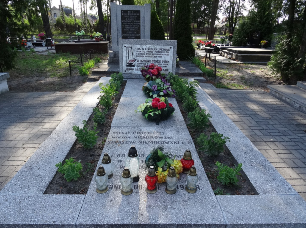 Denkmal in einem Park, das den Opfern der Tschernobyl-Katastrophe gewidmet ist und von Blumen, Kerzen, Bäumen, Gebäuden und einem klaren blauen Himmel umgeben ist.