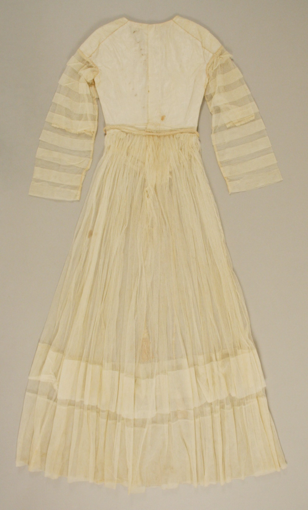 Ein weißes, langärmeliges Kleid mit einer gerüschten, voluminösen Stoffbahn auf einer weißen Oberfläche, das einen dezenten Glanz und eine hohe Taille aufweist.