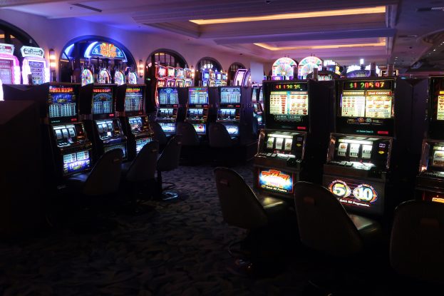Reihe von Spielautomaten in einem Casino mit Stühlen auf dem Boden und Deckenlampen, wobei jedes Gerät Text und Zahlen anzeigt, die darauf hinweisen, dass sie zum Verkauf stehen.