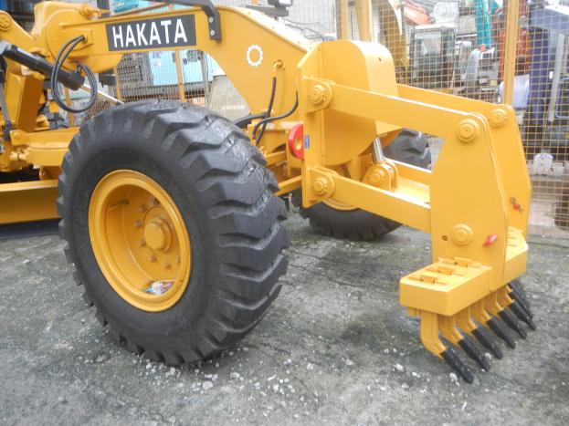 Ein gelber Radlader steht vor einem Gebäude, im Hintergrund ein Metallzaun und ein klarer blauer Himmel.