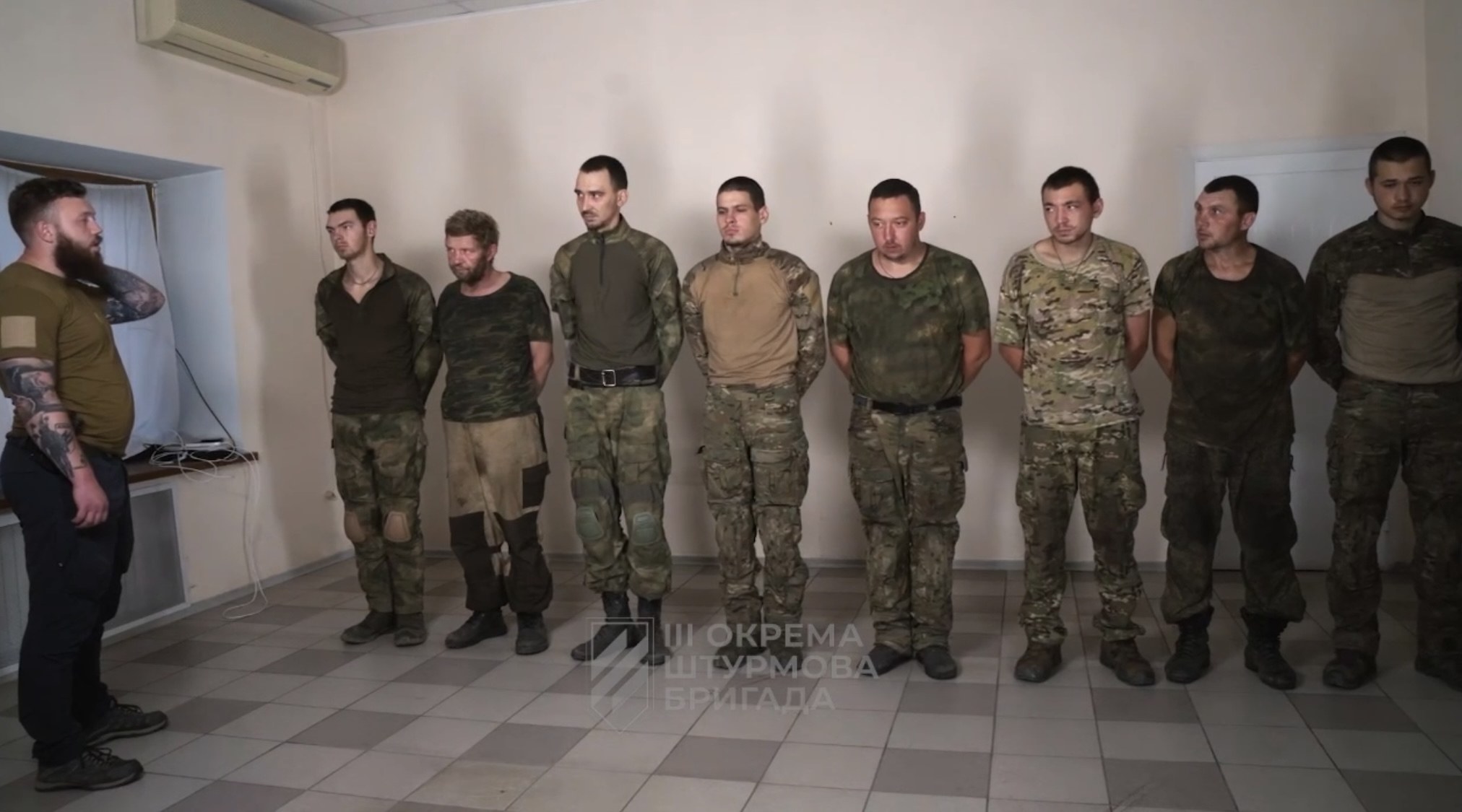 Gruppe von Männern in militärischer Uniform, die in einem Raum mit einer wandmontierten Klimaanlage, einer Tür auf der rechten Seite und einem Tisch mit Gegenständen stehen, mit Text unten, der "Sergei Vorobyov und sein Team" lautet