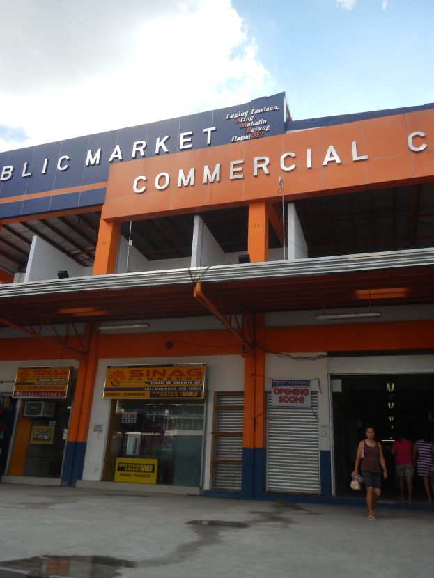 Ein öffentliches Marktgeschäftszentrum mit Menschen davor, Text auf dem Gebäude und ein sichtbarer Himmel oben.