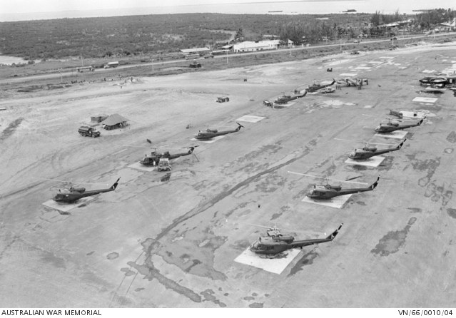 Schwarzes und weißes Foto mehrerer Militärhubschrauber auf dem Boden mit umliegenden Fahrzeugen, Schuppen, Polen, Bäumen und Wasser sowie Text unten.
