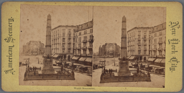 Altes Schwarz-Weiß-Foto einer Straßenansicht mit einem zentralen Denkmal, umgeben von Gebäuden, Straßeneinrichtungsgegenständen, Fahrzeugen und Passanten unter einem sichtbaren Himmel.