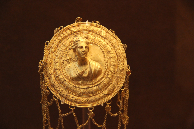 Goldene Medaille mit einer Frauengestalt auf dunklem Hintergrund mit feiner Verzierung und königlichem Aussehen.