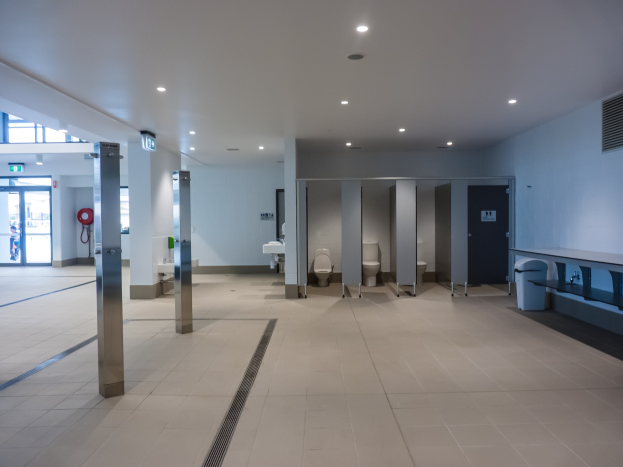 Große Öffentliche Toilette mit mehreren Toiletten, tragenden Säulen, einem Mülleimer, einer Tür, einer Tafel, einem angebrachten Feuerlöscher und Deckenleuchten.