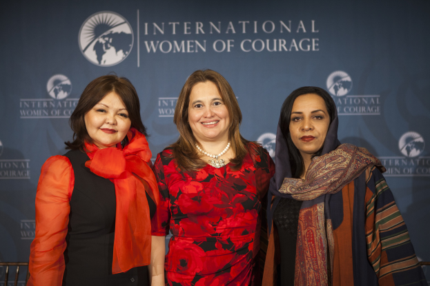 Drei Frauen stehen zusammen vor einem Banner mit der Aufschrift "Internationale Frauen des Mutes".