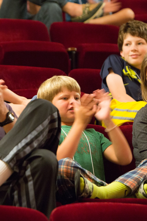 Eine Gruppe von Menschen in einem Kinosaal klatschen, mit einem Jungen in der Mitte umgeben von sitzenden Personen.