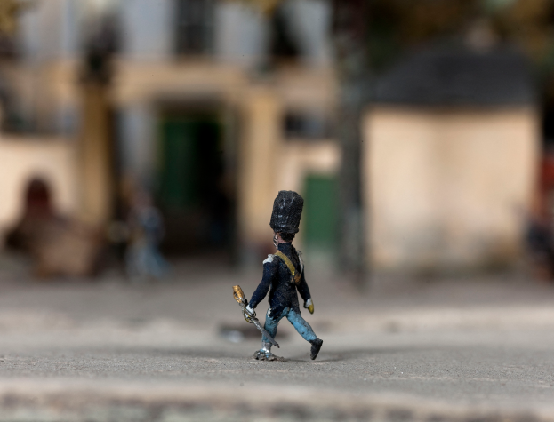 Ein Spielzeugsoldat mit einer Pistole geht die Straße entlang, mit leicht unscharfen Gebäuden im Hintergrund.