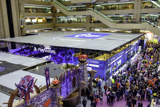 Eine große Menschenmenge in einem großen Konferenzsaal mit Rolltreppen, Geländern, Beleuchtung, Texttafeln und Bannern, mit einem Wasserzeichen, das darauf hinweist, dass es die weltweit größte Gaming-Messe ist.