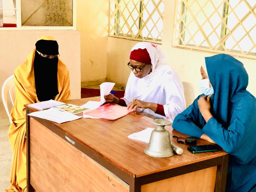 Drei Frauen sitzen an einem unordentlichen Tisch in einem klassenzimmer├Ąhnlichen Setting und diskutieren über Geschlechtergerechtigkeit in Nigeria.