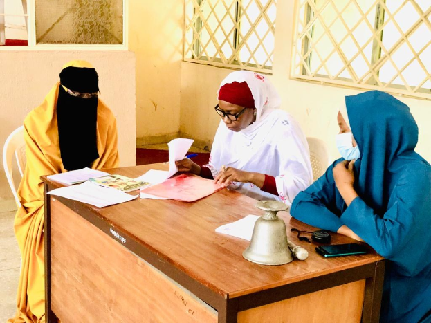 Drei Frauen sitzen an einem unordentlichen Tisch in einem klassenzimmer├Ąhnlichen Setting und diskutieren über Geschlechtergerechtigkeit in Nigeria.