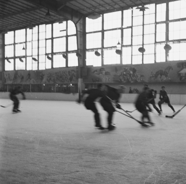 Schwarzes und weißes Foto von Menschen, die Hockey auf einem Eisplatz spielen, mit Gemälden und Fenstern an der Hintergrundwand.