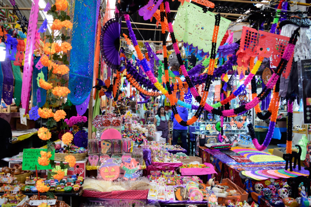 Ein buntes Marktgeschehen mit farbenfrohen Spielzeugen, Dekorationsgegenständen und anderen Waren unter beleuchteter Decke, mit Menschen, die durch die Gänge schlendern und einkaufen.