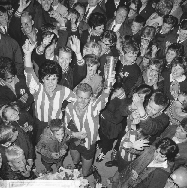 Schwarzes Bild einer Gruppe von Menschen, die mit einem Pokal feiern, die zentrale Figur hält den Pokal, Blumen unten, umgeben von einer Menge.