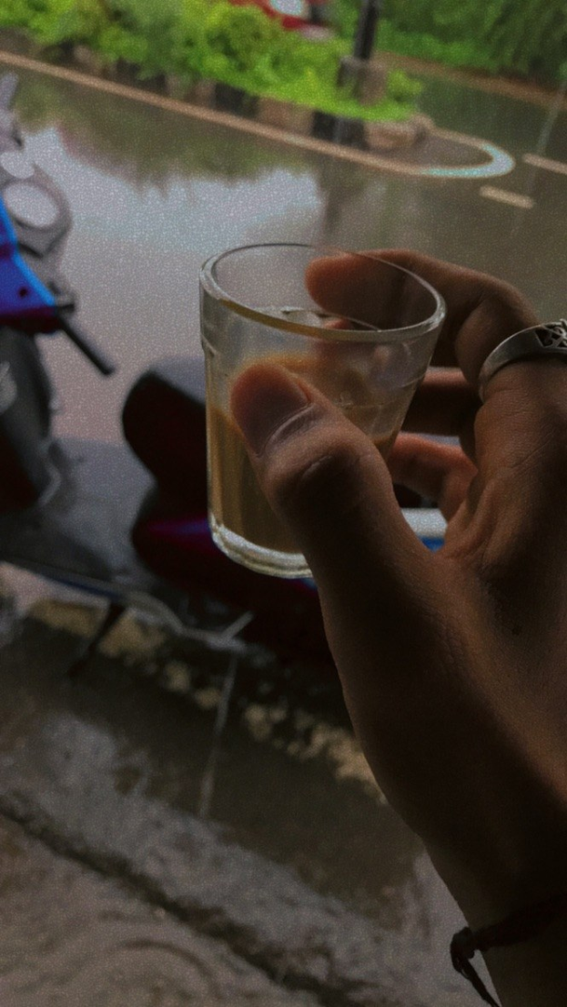 Eine Person mit einem Bierglas vor einem Fenster, daneben ein Motorroller und im Hintergrund Bäume, Pfosten und eine Straße.