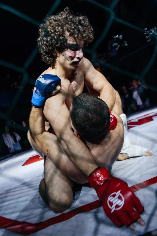 Zwei Männer in einem MMA-Ring, die in einem Kampf gegeneinander antreten, wobei einer einen Tritt gegen den anderen ausführt.