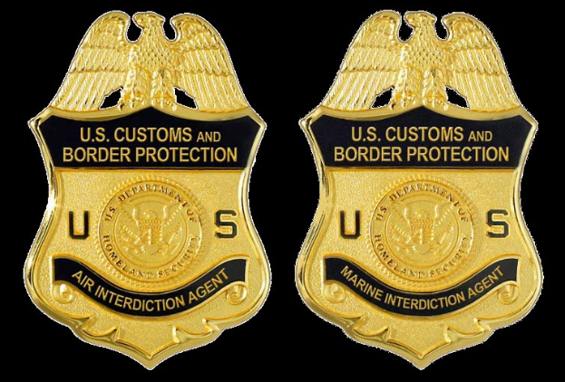 Zwei goldfarbene Abzeichen mit der Aufschrift "U.S. Customs and Border Protection" auf einem weißen Hintergrund.