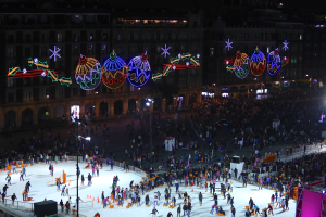 Eine große Menschenmenge, die auf einer Eislaufbahn vor einem Gebäude Schlittschuh läuft, beleuchtet von Straßenlaternen und geschmückt mit festlichen Weihnachtsdekorationen, mit Geländern und Pfosten, die die Bahn umgeben und einem dunklen Hintergrund.