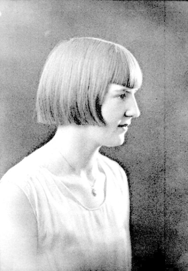Ein Schwarz-Weiß-Foto einer Frau mit einem kurzen Bob-Haarschnitt, ihr Gesicht ist deutlich zu sehen, mit abgewandten Augen und leicht geöffneten Lippen.