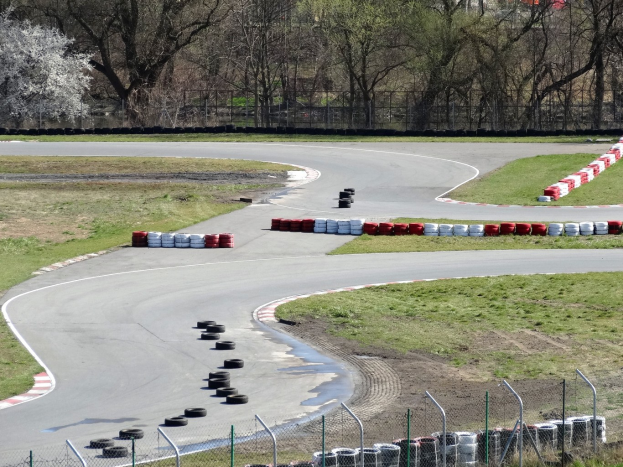 Rennstrecke voller Reifen, umgeben von Gras und Maschendrahtzaun, mit Bäumen im scenischen Hintergrund.