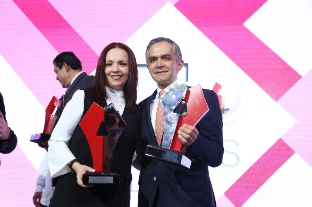 Zwei Menschen lächeln, während sie Trophäen auf einer Bühne halten.