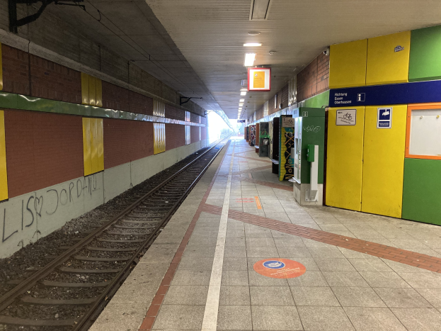 Ein Bahnsteig in Berlin Hauptbahnhof, Deutschland, mit einem stehenden Zug auf den Schienen, Deckenleuchten, die den Bereich beleuchten, Graffiti an einer linken Wand und ein paar Gegenstände auf der rechten Seite.