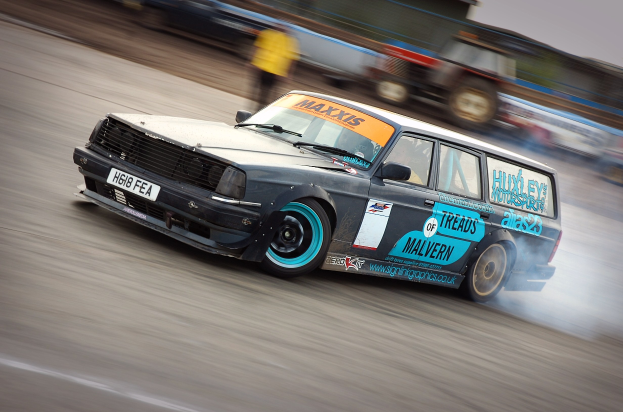 Ein Auto auf einer Rennstrecke, das Rauch ausstöß, umgeben von anderen Fahrzeugen und Zuschauern.