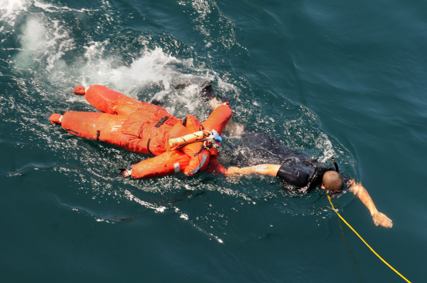Retter in einer orangefarbenen Schwimmweste über einem Gewässer schwebend.