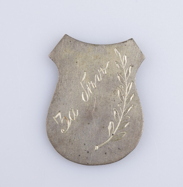 Ein silbern Abzeichen mit einem Lorbeerkranz, darauf die Inschrift "50. Hochzeitstag", auf einem weißen Hintergrund.