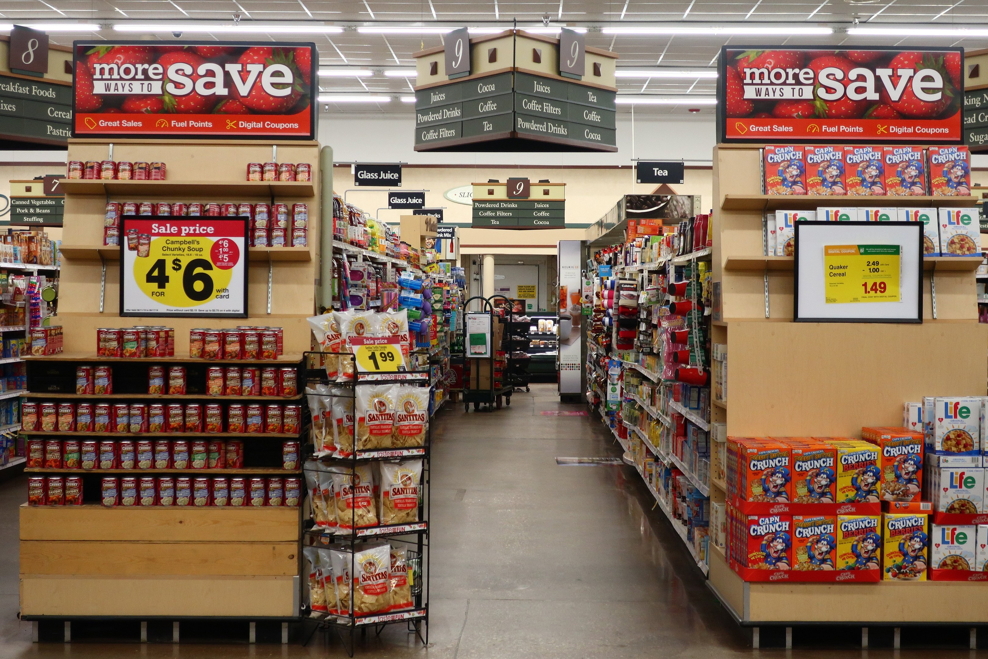 Ein Convenience-Store-Interieur mit Regalen und Boden voller verschiedener Lebensmittel, Deckenbeleuchtung und Informationsschildern, mit einer Person im Hintergrund.