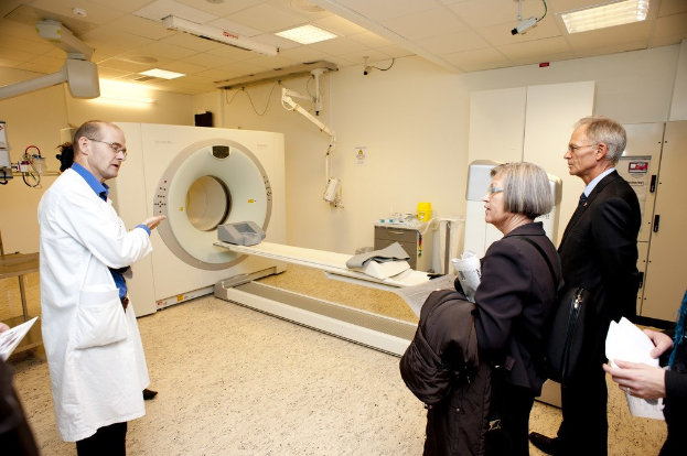Arzt in weißer Uniform erklärt ein CT-Scan-Gerät zwei Personen in schwarzen Mänteln