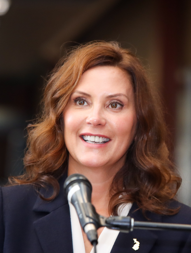 Michele Bachmann, eine Frau im Anzug und mit Krawatte, spricht in ein Mikrofon mit unscharfem Hintergrund.