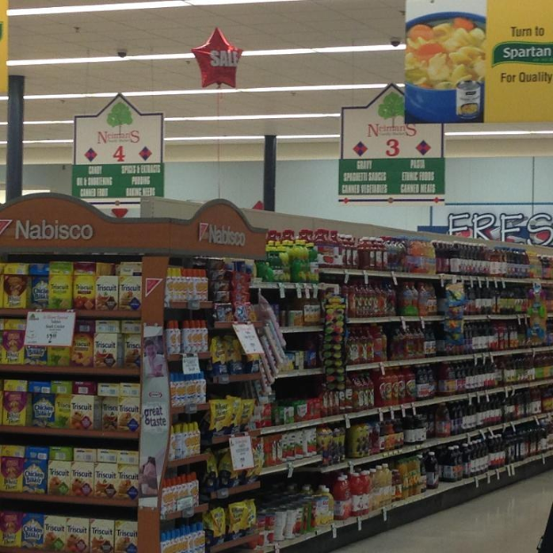 Supermarkt-Innenraum mit deckenmontierten Lampen und Schildern, die Lebensmittel auf Regalen zeigen.