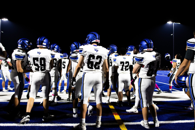 Gruppe von Fußballspielern in Helmen und Stiefeln auf einem Feld unter Flutlicht, bereit für ein Spiel.