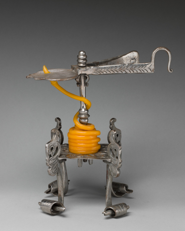 Ein metallener Korkenzieher mit einer hellgelben Feder an seiner Oberseite, der einen zylindrischen Körper, einen Griff an einer Seite und einen Ausguss an der anderen Seite aufweist.