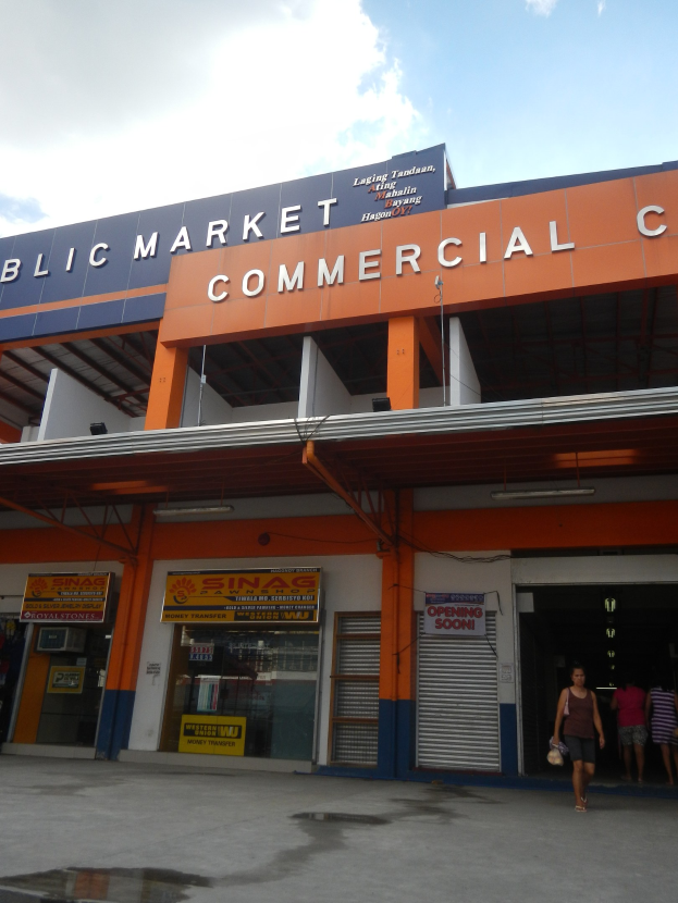 Öffentlicher Markt mit Menschen vor einem Gebäude mit Text, unter einem sichtbaren Himmel.